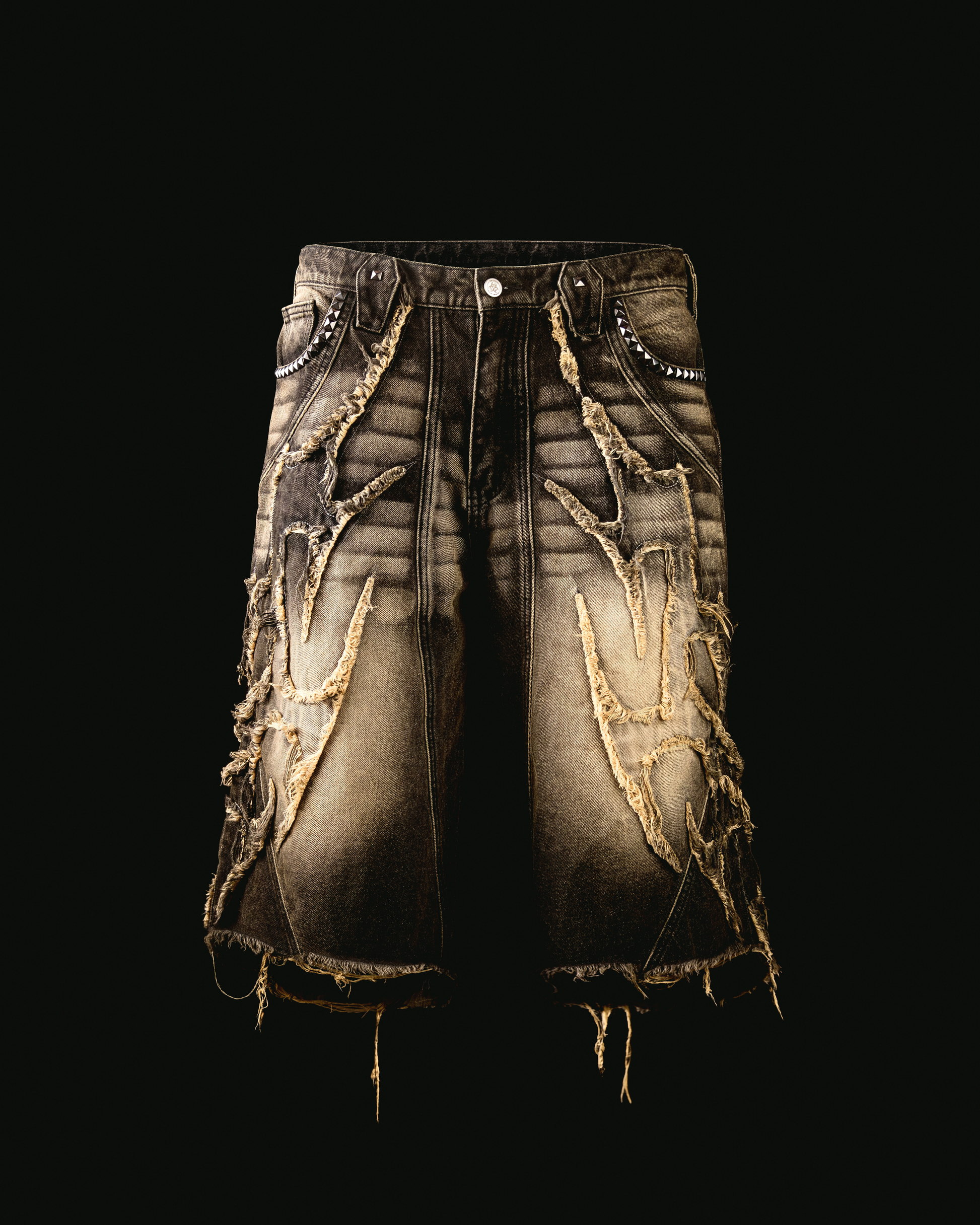 A pair of men's denim shorts with a special desert wash treatment, featuring frayed bottom hem look and pyramid studs metal hardware on the front and back.